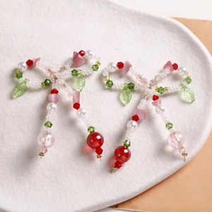 Detailed macro of handmade bow earrings with faux pearls, green leaves and colorful beads