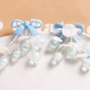 Close-up of light blue resin bow earrings with iridescent beaded tassels on a tray