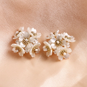 Primo piano di orecchini a fiore bianco perla con centri di perline dorate lucide