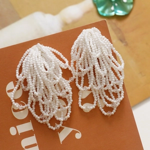 Detailed view of handmade cream white beaded fringe earrings with layered tassel design