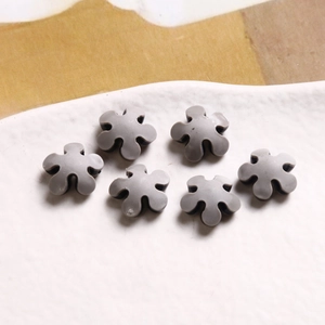 Detailed view of six gray acrylic flower pendants for DIY jewelry making on white ceramic