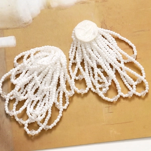 Detailed view of white beaded tassel earrings with crystal pendants on a vintage background