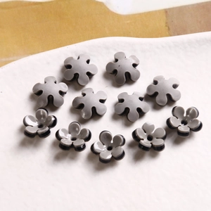 Macro detail of bicolor five-petal flower charms in grey and black acrylic on a tray