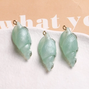 Three light green resin conch shell pendants with gold loops on a textured white plate
