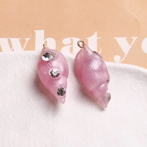 Macro detail of conch-shaped resin charms with crystal accents and gold hoops