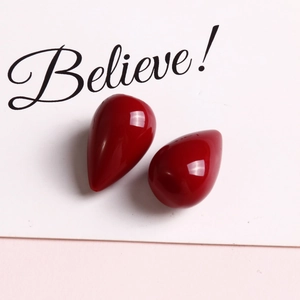Close-up of glossy red teardrop resin charms for DIY jewelry on a card backdrop