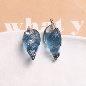 Detail of blue resin conch charm with white rhinestones and a golden metal ring