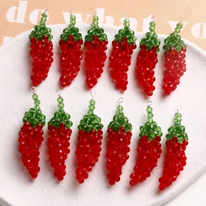 Macro detail of handmade red glass chili pendants on a white ceramic tray for DIY jewelry