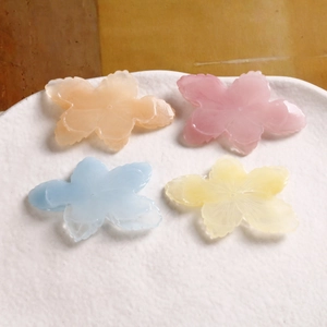 Pastel resin five-petal flower charms in pink yellow and blue on a ceramic plate