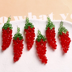 Close-up of six handmade red and green chili-shaped beaded pendants on a white plate
