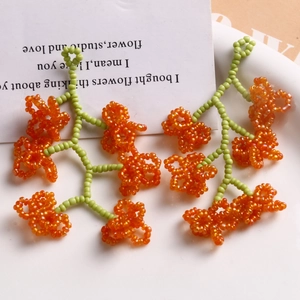 Pendentif fleur en perles de verre fait main avec pétales orange et tiges vertes sur assiette