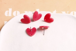 Détails macro des boucles d'oreilles cœur en acrylique magenta brillant sur plateau