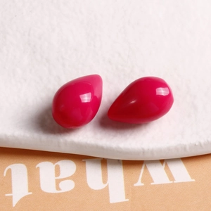 Detail of high-gloss rose red teardrop resin charms on a textured stone display