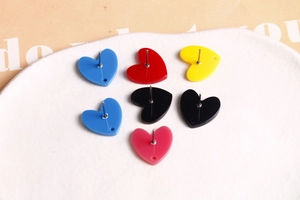 Vue macro de boucles d'oreilles cœur en acrylique coloré avec tiges en métal sur un plateau