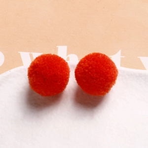 Close-up of vibrant orange fluffy plush pom-pom charms on a white textured plate