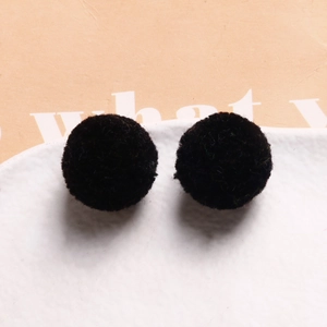 Detail view of pair of 20mm soft black plush pom-poms on a white ceramic plate
