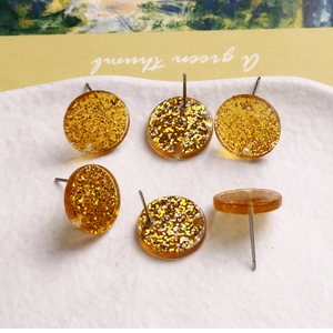 Detailed macro view of golden glitter resin earrings with silver foil in a ceramic dish