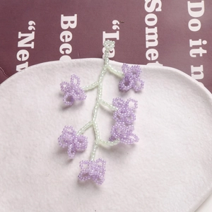 Pendentif fleur en perles violettes fait main avec touches vertes dans un plat blanc