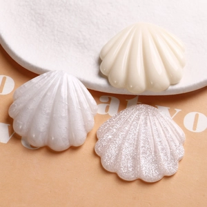 Détail de trois breloques coquillages en résine aux finitions nacrées et pailletées pour loisirs