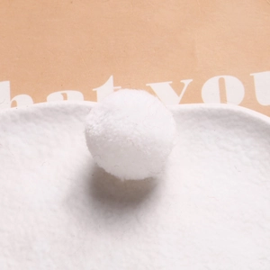 Macro shot of a soft white 20mm plush pom pom on a textured white ceramic plate