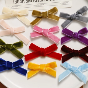 Close-up display of twelve colorful velvet bow hair clips on a minimalist white tray