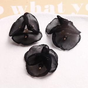 Tres flores de malla negra hechas a mano con perlas doradas en un plato de cerámica blanca