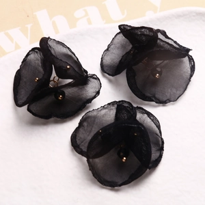 Detalle de tres flores de malla negra con cuentas doradas y anillos de metal para joyas