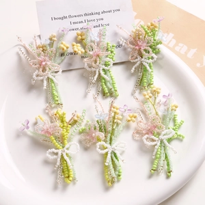 Detail of six handmade green beaded floral charms with pink centers and white bows