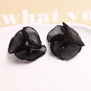 Detalle de pendientes de flores de malla negra con cuentas doradas en plato blanco