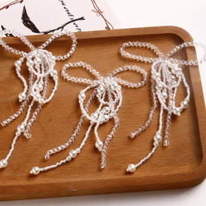 Detailed view of handmade pearl bow charms with tassels on a rustic wooden tray