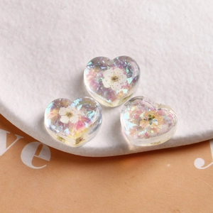 Macro detail of transparent resin heart charms with dried white flowers and laser sequins