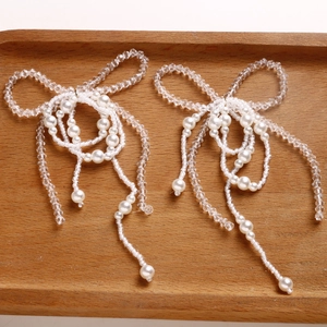 Close-up of handmade pearl bow and crystal bead tassel accessory on wood background