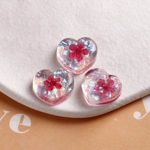 Close-up of three pink resin heart charms with dried flowers and iridescent glitter