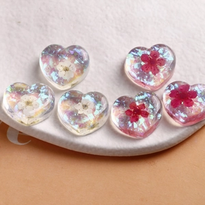 Detail of 6 resin heart charms with dried flowers and gold foil on a ceramic plate