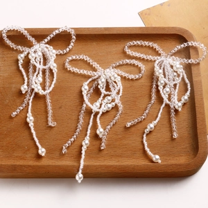 Detailed view of three handmade woven pearl bow pendants with tassels on wooden tray