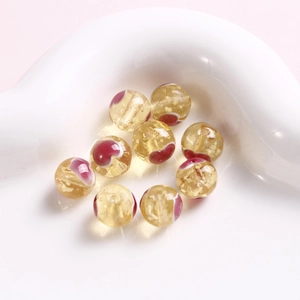 Detailansicht von 10 mm gelben Glasperlen mit rotem Herzmuster und Goldfolie