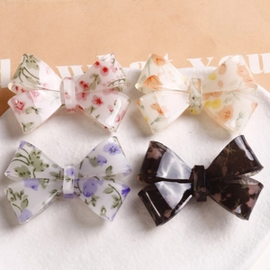 Flat lay detail of four acetate floral bow hair clips on a white ceramic plate