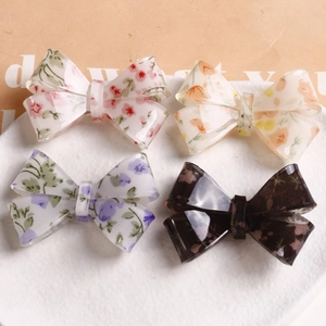 Detail shot of four floral bow hair clips in pink and purple on a white textured ceramic plate