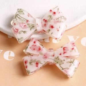 Close-up of clear resin bow charms with embedded pink flowers and green leaves