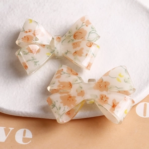 Detailed view of floral resin bow hair clips with soft orange blossom patterns