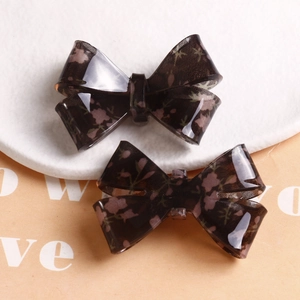 Detail of resin bow charms with delicate floral pattern and black grid texture