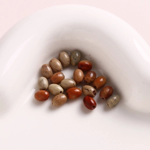 Detailed view of 6mm oval natural stone beads with drill holes in a white ceramic bowl