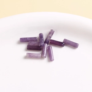 Macro detail of cylindrical purple natural stone beads with crackle texture in a white tray