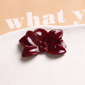 Macro shot of glossy burgundy resin flower charm for jewelry making on ceramic plate