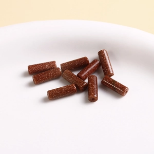 Macro shot of 9 reddish-brown goldstone cylinder beads on a white ceramic tray