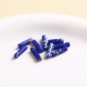 Macro shot of blue marble pattern cylindrical beads on a white ceramic tray for DIY jewelry