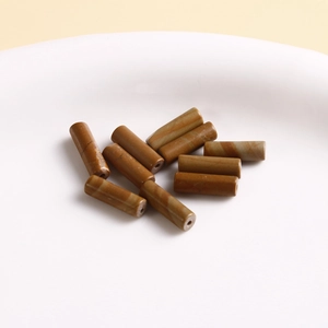 Close-up of cylindrical natural stone beads with brown marbled texture in a white bowl