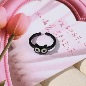 Dettaglio anello gatto nero con grandi occhi su uno sfondo floreale rosa chic