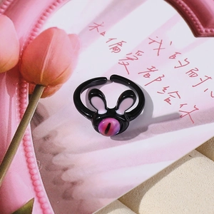 Dettaglio dell'anello nero a forma di coniglio con orecchie rosa e occhio viola su fiori