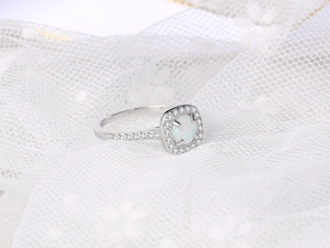 Macro view of cushion cut white opal ring with halo diamonds on white lace background